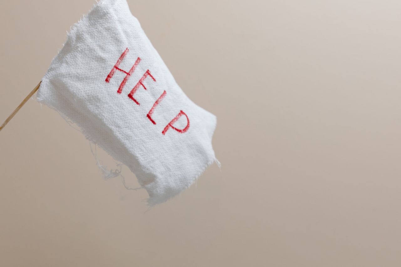 A white flag with HELP displayed on a beige background, symbolic of seeking assistance.